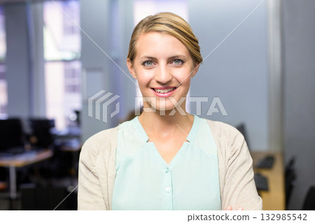 Female office professional standing and smiling at modern office with desks monitors and keyboard Female office professional standing and smiling at modern office with desks monitors and keyboard 132985542