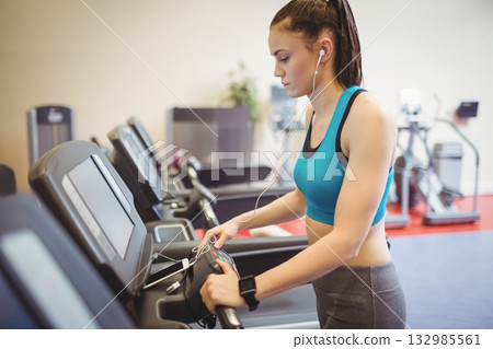 Woman wearing teal sports bra and gray leggings adjusting treadmill console at gym, copy space Woman wearing teal sports bra and gray leggings adjusting treadmill console at gym, copy space 132985561