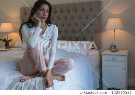 Asian woman sitting on bed in bedroom resting chin and gazing to side by tufted headboard Asian woman sitting on bed in bedroom resting chin and gazing to side by tufted headboard 132985581