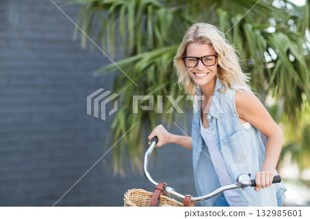 Woman wearing eyeglasses standing beside bicycle with wicker basket on garden path, copy space 132985601