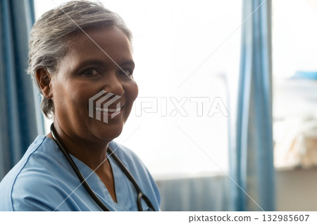 Senior African American healthcare worker standing by clinic window wearing scrubs and stethoscope Senior African American healthcare worker standing by clinic window wearing scrubs and stethoscope 132985607