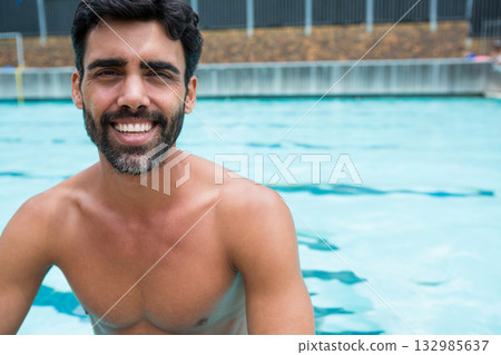 Man leaning against concrete edge with pool water, metal fence at pool wearing trunks, copy space Man leaning against concrete edge with pool water, metal fence at pool wearing trunks, copy space 132985637