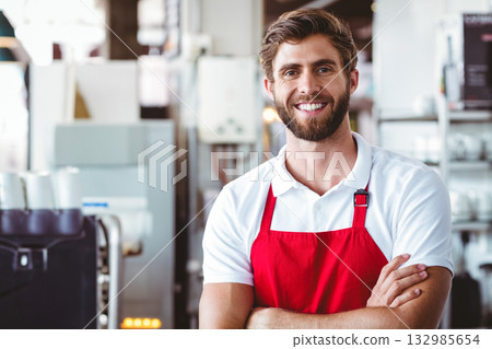 Man wearing red apron smiling beside coffee machine in coffee shop kitchen, copy space 132985654