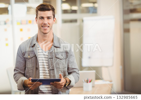 Man standing in office wearing denim jacket holding tablet beside flip chart with sticky notes Man standing in office wearing denim jacket holding tablet beside flip chart with sticky notes 132985665