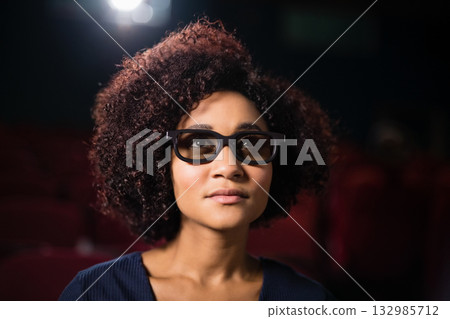 African American woman watching 3D film through dark-framed glasses in dim cinema hall African American woman watching 3D film through dark-framed glasses in dim cinema hall 132985712