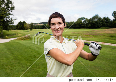 Woman standing on golf course fairway holding golf club over shoulders wearing glove and polo shirt Woman standing on golf course fairway holding golf club over shoulders wearing glove and polo shirt 132985717