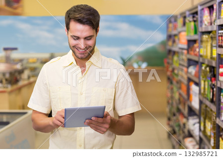 Man holding tablet and checking grocery prices while standing in supermarket aisle Man holding tablet and checking grocery prices while standing in supermarket aisle 132985721