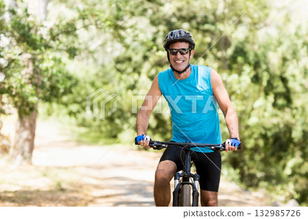 Middle-aged man riding mountain bike on sunlit forest trail wearing helmet sunglasses blue jersey Middle-aged man riding mountain bike on sunlit forest trail wearing helmet sunglasses blue jersey 132985726