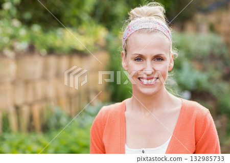 Blonde woman standing by picket fence wearing floral headband amid shrubs and foliage, copy space Blonde woman standing by picket fence wearing floral headband amid shrubs and foliage, copy space 132985733