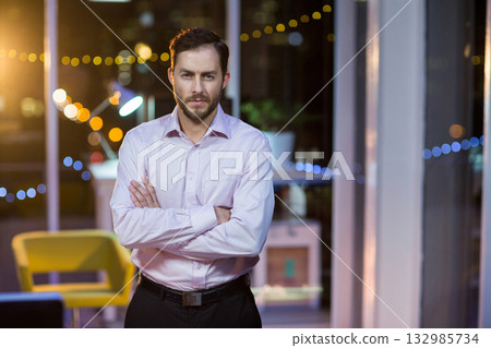 Mid adult man standing in office lounge at night wearing business attire by string lights 132985734
