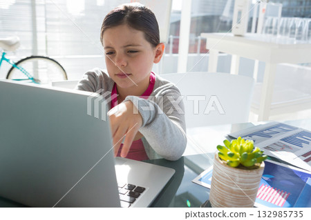 Female child studying on laptop in home office with succulent plant and charts beside bicycle wheel Female child studying on laptop in home office with succulent plant and charts beside bicycle wheel 132985735