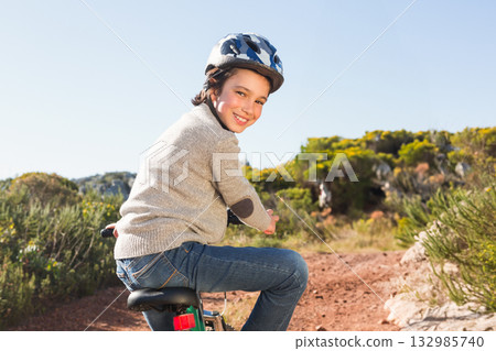 Boy wearing patterned helmet and sweater riding bicycle along dusty trail in scrub under blue sky Boy wearing patterned helmet and sweater riding bicycle along dusty trail in scrub under blue sky 132985740