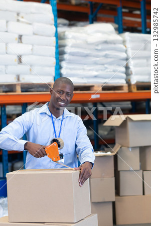 African American man in light blue shirt sealing box with tape dispenser at warehouse shelving African American man in light blue shirt sealing box with tape dispenser at warehouse shelving 132985742