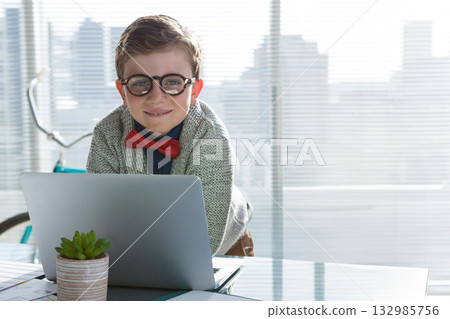 Boy student leaning forward over desk by office windows working on laptop near bicycle 132985756