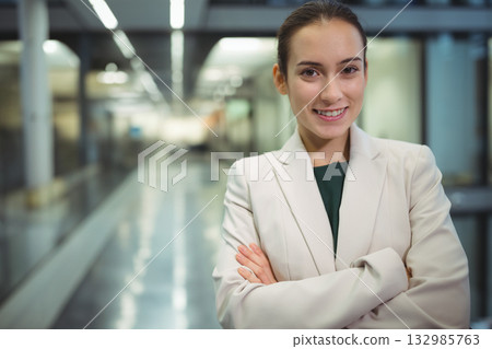 Professional woman folding arms facing camera in corporate corridor with glass walls, copy space 132985763