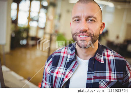 Mid adult man smiling while typing on keyboard near desk in open-plan office, copy space Mid adult man smiling while typing on keyboard near desk in open-plan office, copy space 132985764