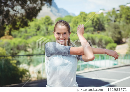 Woman stretching arm across chest on outdoor sports court with fence railing and court lines Woman stretching arm across chest on outdoor sports court with fence railing and court lines 132985771