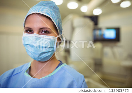 Female surgeon standing in operating room wearing scrub suit, mask and cap with imaging device Female surgeon standing in operating room wearing scrub suit, mask and cap with imaging device 132985775