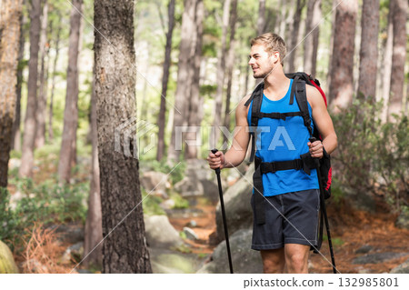 Man hiking rocky trail in pine forest gripping trekking poles and carrying backpack, copy space 132985801
