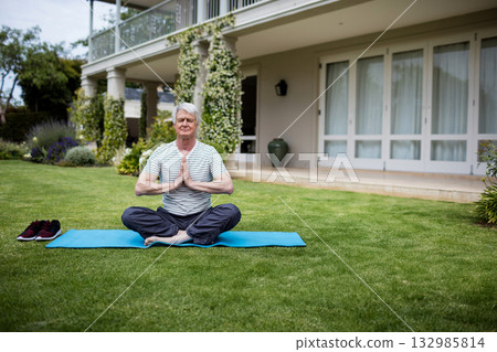White senior man practicing yoga on blue mat on backyard lawn with columns wrapped in vines White senior man practicing yoga on blue mat on backyard lawn with columns wrapped in vines 132985814