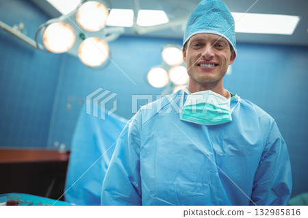 Male surgeon in blue scrubs standing under surgical lights in operating room, copy space Male surgeon in blue scrubs standing under surgical lights in operating room, copy space 132985816
