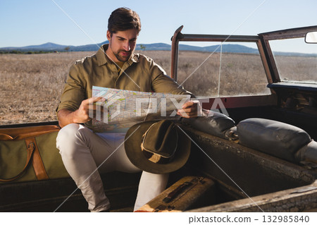 Man sitting in pickup cargo area studying paper map with brown hat, duffel bag and suitcase Man sitting in pickup cargo area studying paper map with brown hat, duffel bag and suitcase 132985840