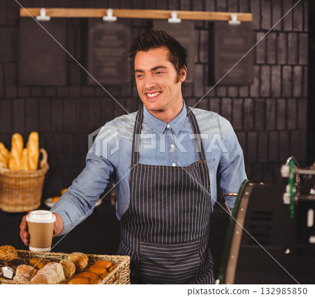 Male barista handing coffee cup forward behind bakery counter with bread baskets and menu boards 132985850