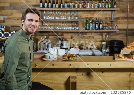 Man sitting at bar counter at cafe drinking coffee with sandwich plate and stirrers, copy space 132985870