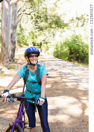 Senior woman riding purple mountain bike on woodland trail, wearing helmet, sunglasses and backpack 132985877