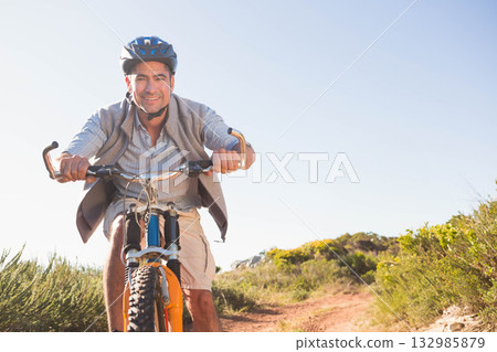 Male cyclist wearing blue helmet riding mountain bike along dusty trail amid shrubs under clear sky Male cyclist wearing blue helmet riding mountain bike along dusty trail amid shrubs under clear sky 132985879