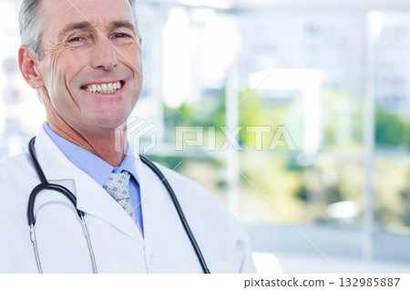 Senior male doctor standing beside window in clinic wearing white coat with stethoscope, copy space Senior male doctor standing beside window in clinic wearing white coat with stethoscope, copy space 132985887