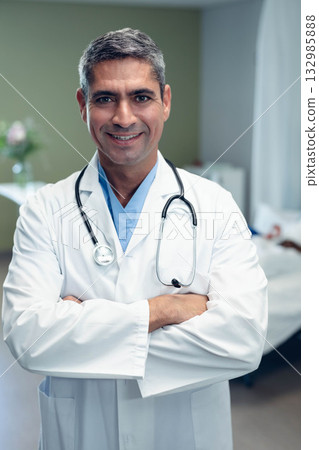 Senior male doctor standing in hospital room wearing lab coat and stethoscope beside patient bed Senior male doctor standing in hospital room wearing lab coat and stethoscope beside patient bed 132985888