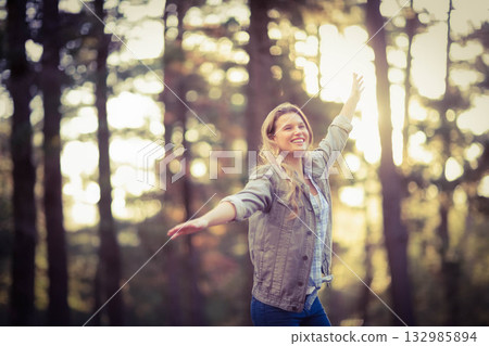 Woman standing arms outstretched in golden forest clearing wearing plaid shirt olive jacket jeans Woman standing arms outstretched in golden forest clearing wearing plaid shirt olive jacket jeans 132985894