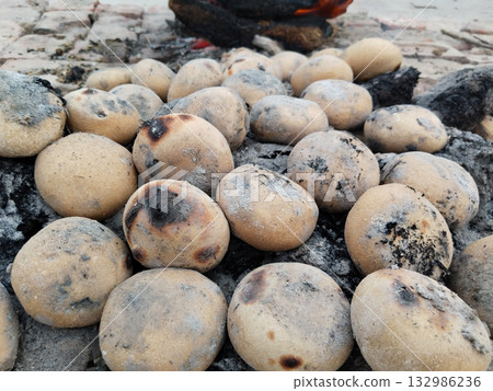 Round wheat flour balls being roasted on residual ashes of burnt cow dung cakes in traditional Indian village method, showing post-fire slow cooking technique used for preparing litti 132986236