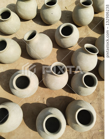 Multiple raw clay matkas arranged outdoors under direct sunlight for drying, top view of traditional earthen pots in rural pottery scene Multiple raw clay matkas arranged outdoors under direct sunlight for drying, top view of traditional earthen pots in rural pottery scene 132986238