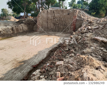 Small Bridge Under Construction on Village Road for Irrigation Water Flow Reflecting Rural Life and Agricultural Development with Dug Earth and Fields Under Cloudy Sky Surrounded by Houses and Green 132986249