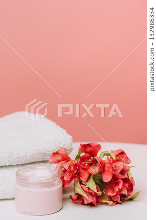 Pink face cream jar with flowers and towels on coral background Pink face cream jar with flowers and towels on coral background 132986334