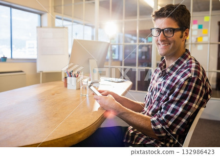 Mid-adult man sitting in office holding smartphone amid monitor pen holder sticky notes, copy space Mid-adult man sitting in office holding smartphone amid monitor pen holder sticky notes, copy space 132986423