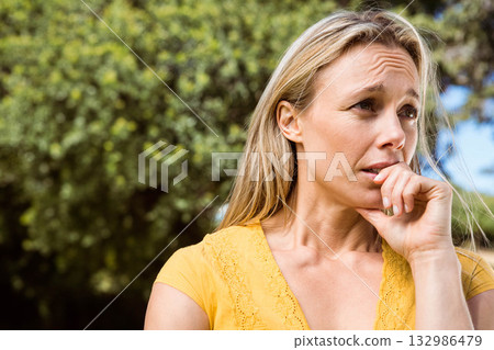 Woman standing outdoors by dense green foliage in yellow lace-trimmed top raising hand to mouth Woman standing outdoors by dense green foliage in yellow lace-trimmed top raising hand to mouth 132986479