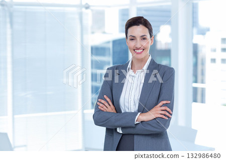Woman in grey blazer striped blouse standing with arms crossed at office windows city view 132986480