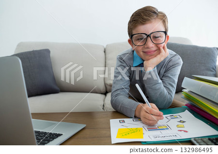 School-age boy drawing diagrams at coffee table in living room with pen and laptop, copy space School-age boy drawing diagrams at coffee table in living room with pen and laptop, copy space 132986495