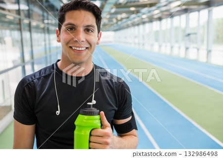 Male athlete in black shirt standing on track holding green water bottle with earphones, copy space Male athlete in black shirt standing on track holding green water bottle with earphones, copy space 132986498