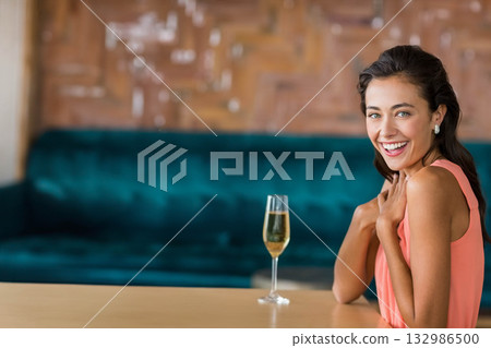Woman sitting in lounge wearing coral top holding champagne glass on wooden table, copy space Woman sitting in lounge wearing coral top holding champagne glass on wooden table, copy space 132986500