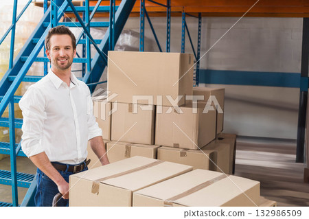 Man pushing hand truck loaded with cardboard boxes on concrete floor in warehouse, copy space Man pushing hand truck loaded with cardboard boxes on concrete floor in warehouse, copy space 132986509