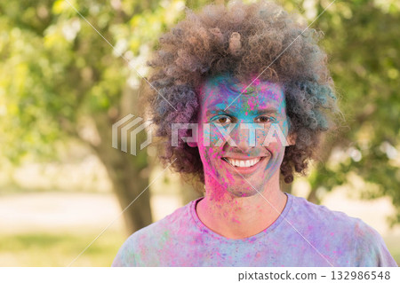 Curly-haired adult man grinning while standing in park with powder-covered T-shirt and face Curly-haired adult man grinning while standing in park with powder-covered T-shirt and face 132986548