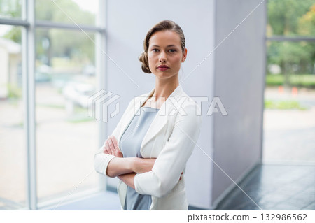 Woman in blazer standing crossing arms by pillar in office lobby facing parked car past windows8691 132986562