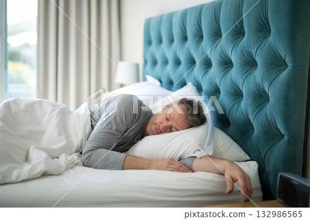 Mature man sleeping on side in master bedroom on white pillow under duvet, copy space 132986565
