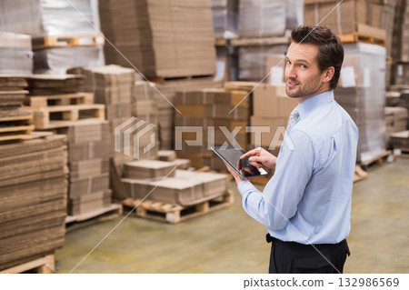Man in shirt and tie holding tablet while inspecting inventory on pallets in warehouse, copy space 132986569