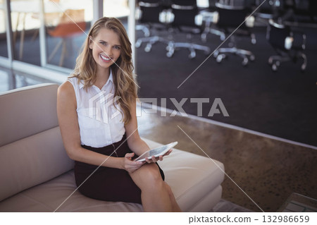 Woman sitting on leather sofa by glass partition in office lounge holding tablet, copy space 132986659