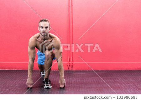 Male athlete starting sprint on rubber floor near red wall, wearing blue shorts and sneakers 132986683